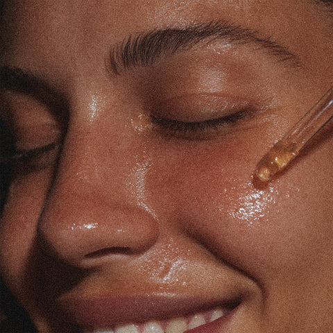 Close-up of a person applying a dropper of liquid to their face.