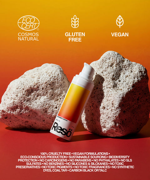 A Vitamin C Serum bottle is positioned between two white rocks on a red surface with a yellow-orange gradient background. Icons and text emphasize its certifications: EcoCert, gluten free, vegan, and clean beauty claims.