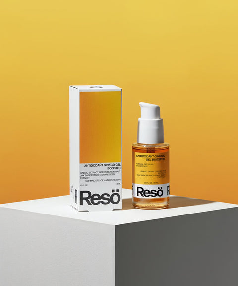 A bottle of Antioxidant Ginkgo Gel Booster with a white pump stands by its box on a white pedestal against a bold yellow gradient. This oil-free gel contains ginkgo extract and offers pollution protection for radiant skin.