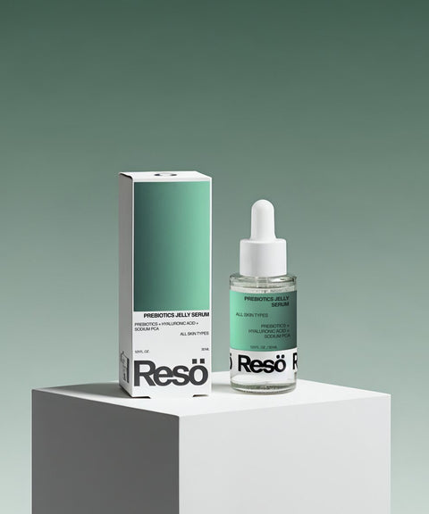 A bottle of RESÖ Bioactive Prebiotics Jelly Serum with a white dropper cap stands beside its matching green and white box on a white pedestal, set against a green gradient background, emphasizing soothing hydration and barrier repair.