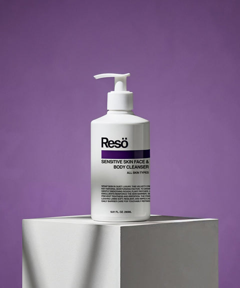 A white pump bottle of RESÖ Sensitive Skin Face & Body Cleanser, a gentle gel for all skin types, stands on a white pedestal against a purple background.