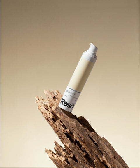 A cylindrical bottle of RESÖ Nourishing Rich Cream, Fragrance Free, stands upright on textured, weathered wood against a neutral beige gradient background—ideal for soothing dry skin.