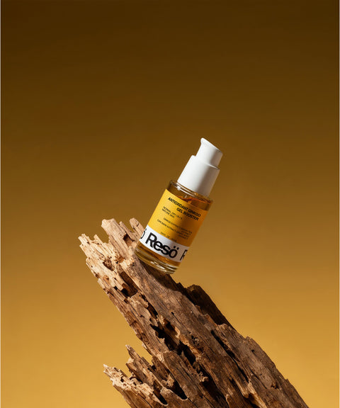 A glass bottle of Antioxidant Ginkgo Gel Booster with a white pump sits on weathered wood, offering pollution protection with potent ginkgo extract against a brown and gold gradient background.