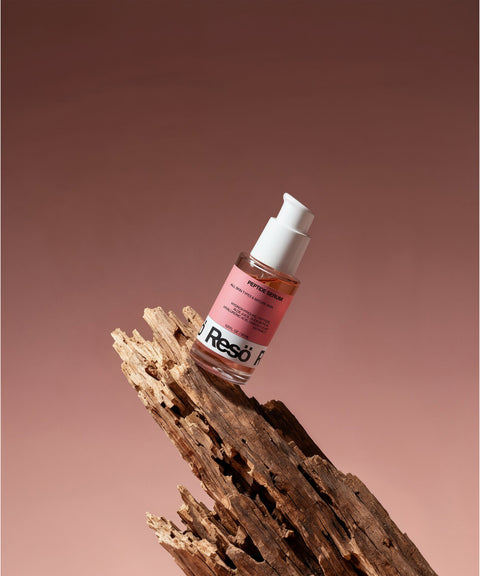 A pink bottle of Peptide Anti-Aging Serum rests on textured, weathered wood with a gradient pink and brown background.