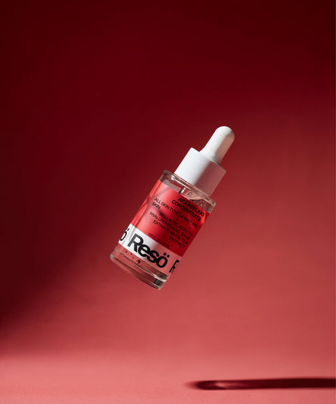 A glass dropper bottle containing a red liquid labeled “Reso” is suspended against a red gradient background, with a white cap and dropper. The bottle appears to be floating in mid-air.