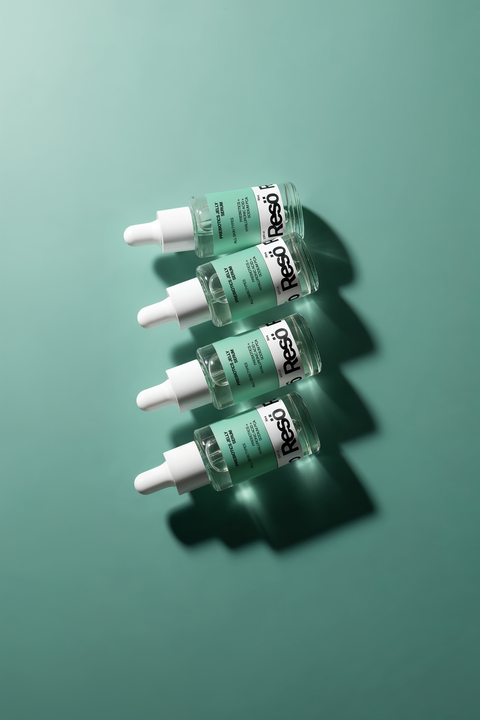Four glass dropper bottles with green labels and white caps are arranged diagonally on a teal background, casting shadows to the right. The labels read Reso and contain additional text.