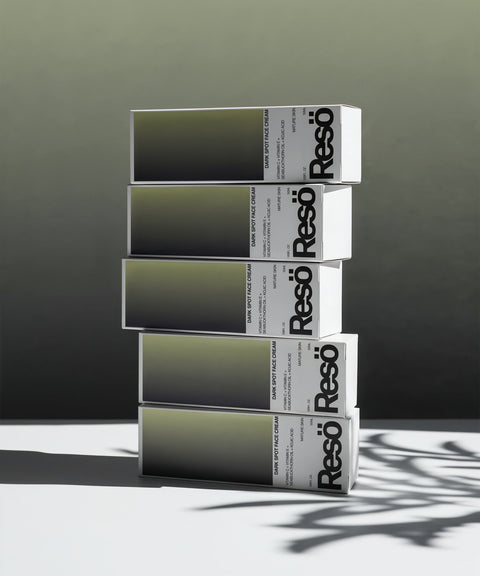 Five rectangular boxes labeled Reso are stacked in a staggered, leaning arrangement. The boxes have a minimalist design with gray and white gradients and bold black text. A leaf shadow is visible on the surface.
