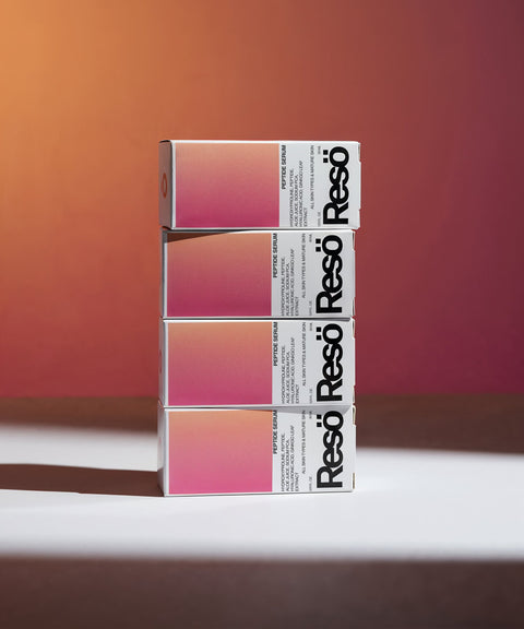 Three stacked rectangular boxes with a gradient pink and orange design and bold black “Resö” text on the side, set against a warm red and brown background with dramatic lighting.