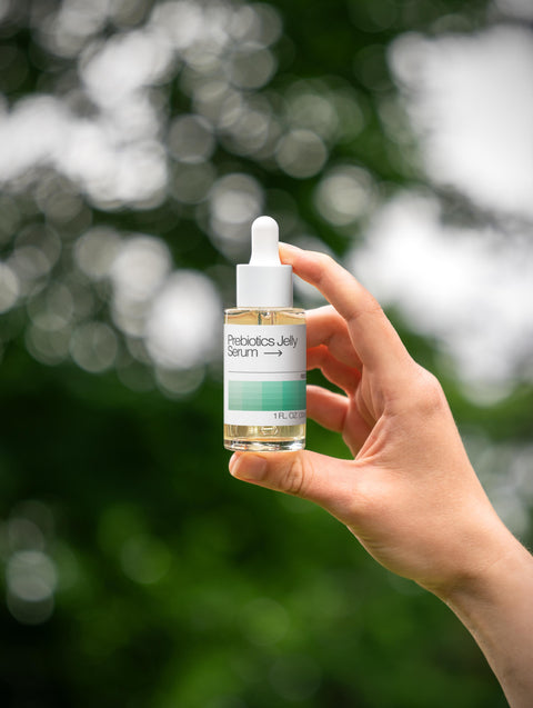 Hand holding a bottle of 'Probiotic Jelly Serum' against a blurred natural background
