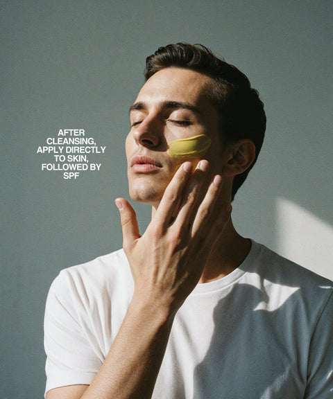 A man in a white shirt applies RESÖ Vitamin C Serum to his cheek with eyes closed. Text reads: After cleansing, apply directly to skin, followed by SPF. Sunlight creates a shadow on the wall behind.