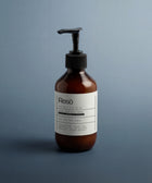 A brown pump bottle labeled Resö sits on a blue-gray surface. The label describes Silk Skin Body Serum, Woody Amber & Leather, hydrating for all skin types with squalane, jojoba oil, bakuchiol, and ginkgo extract.