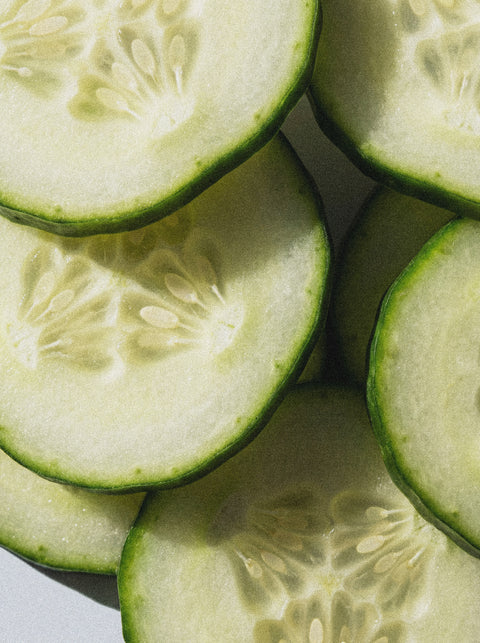 Close-up of overlapping cucumber slices, their fresh, juicy texture evoking the hydration and softness you feel after applying the 5% Urea + 2% Panthenol Body Cream. Bright light highlights their crispness, symbolizing skincare refreshment.