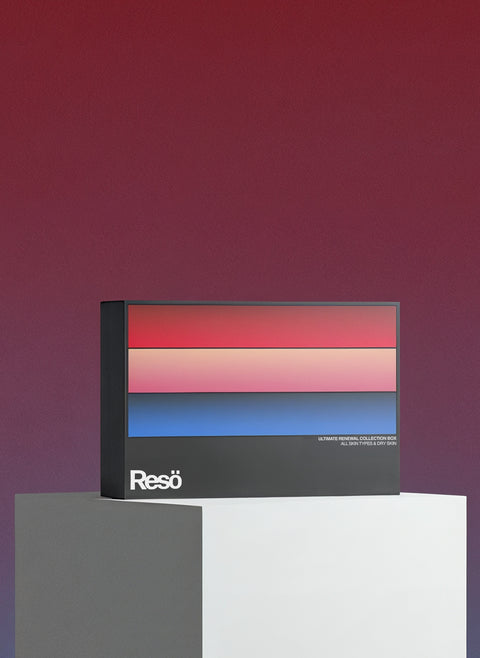 A rectangular box with red, pink, purple, and blue stripes stands on a white surface against a red-purple gradient background. "RESÖ" is in white text at the bottom left. It's The Ultimate Renewal Collection Box for radiant skin.
