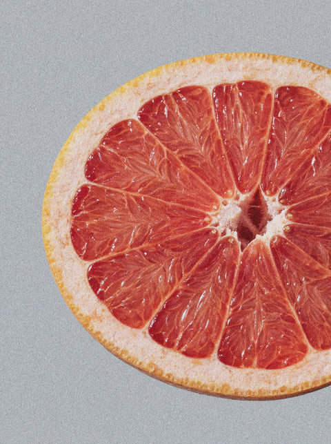 A close-up of Hand & Body Wash, Grapefruit features bright red grapefruit flesh and a yellow rind against a light gray background, capturing the juicy segments and refreshing grapefruit essence of the product.
