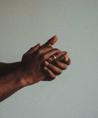 A close-up of two hands clasped together, one adorned with a simple ring, bathed in soft light that highlights the nourished skin—showcasing the gentle care of Silk Skin Hand Cream, Woody Amber & Leather.