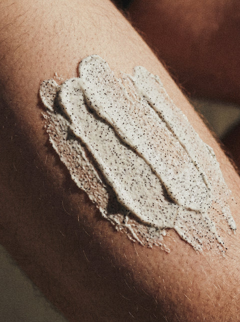 A close-up of a person’s arm with Icelandic Volcano Face & Body Scrub applied—white cream infused with mineral exfoliant granules and visible specks throughout for deep cleansing.