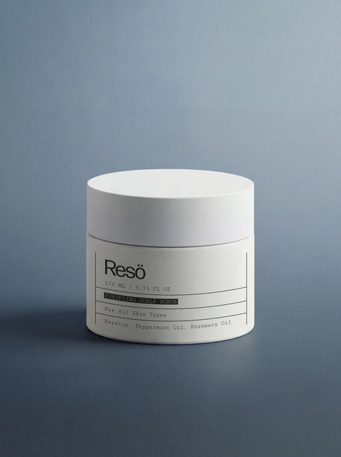 A white cylindrical jar labeled “Resö” contains Deep Cleanse Scalp Scrub, Rosemary & Mint—an exfoliating treatment with keratin, peppermint oil, and rosemary oil for all skin types—displayed against a gradient gray-blue background.