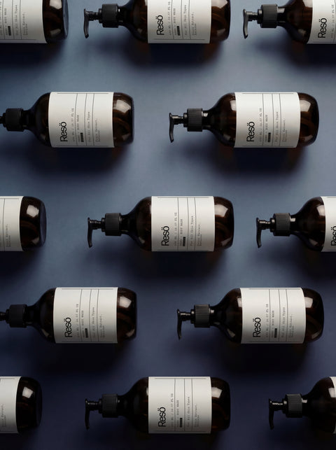 Several brown glass pump bottles with white labels are arranged in a neat, alternating horizontal pattern on a smooth, blue-gray surface. The labels read Reso and contain minimal, modern text.
