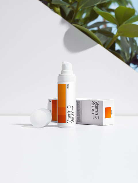 Vitamin C serum packaging on a white surface with green leaves in the background